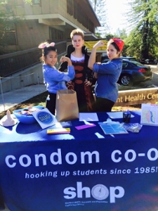 Three students posing with a condom co-op tablecloth and table set-up
